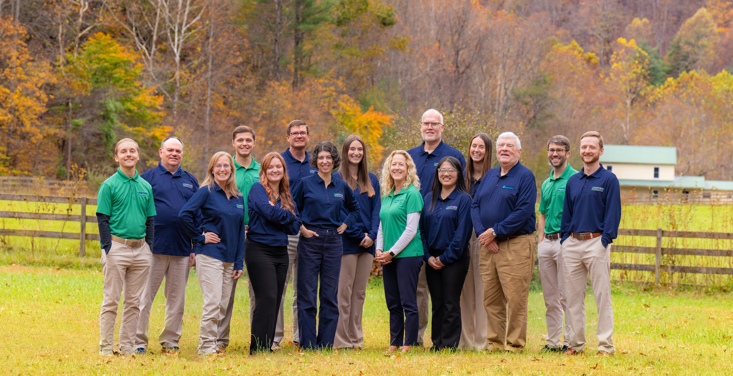 A group of employees standing in a field with a fence in the background.